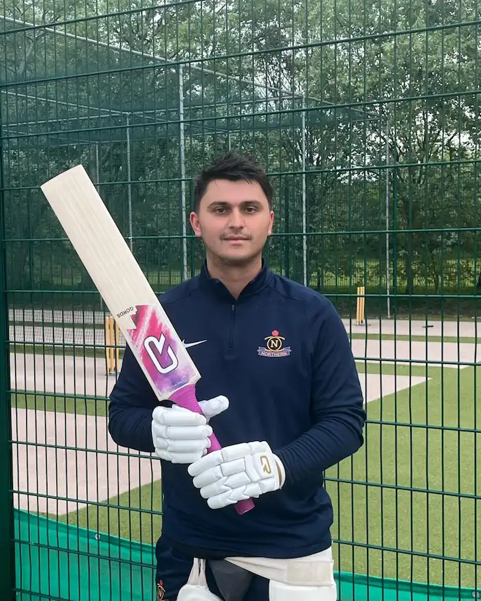 Cricket player in navy uniform holding pink and white CR cricket bat at practice nets