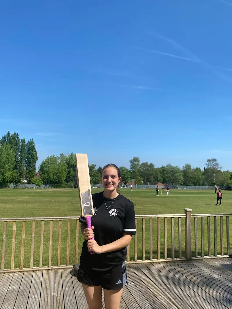 Female cricket player holding CR cricket bat with pink grip at outdoor cricket ground on sunny day